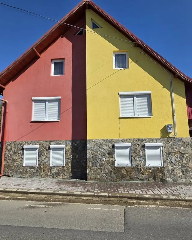 Casă cu fațadă galbenă și roșie și soclu din piatră, după spălarea fațadei